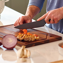 Manos sosteniendo un cuchillo y cortando verduras en tabla de madera
